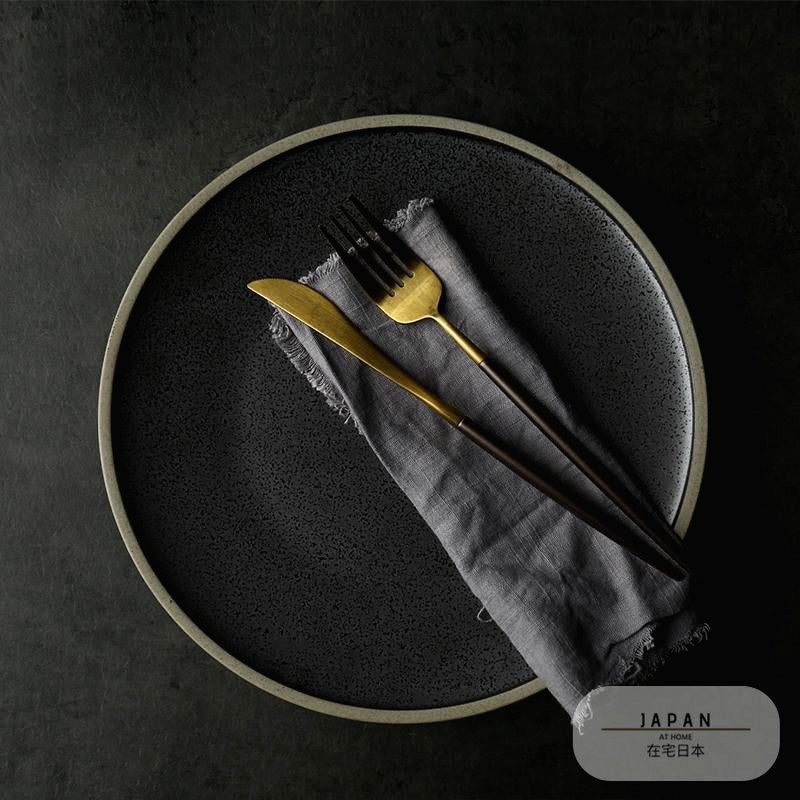 Assiette Inoue noire à bord clair avec serviette et couverts dorés
