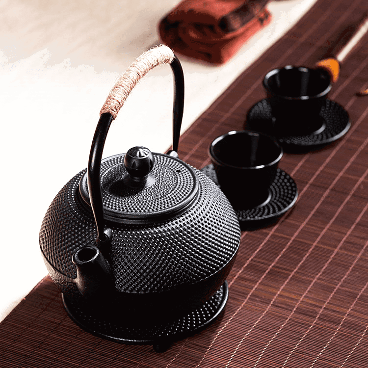 Théière en fonte Murata sur son dessous de plat, tasses sur un chemin de table